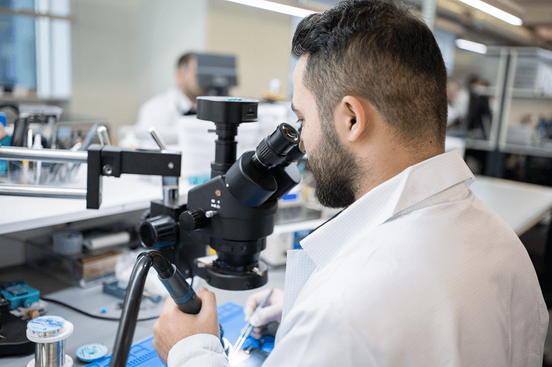Technician inspecting a board under a stereo microscope